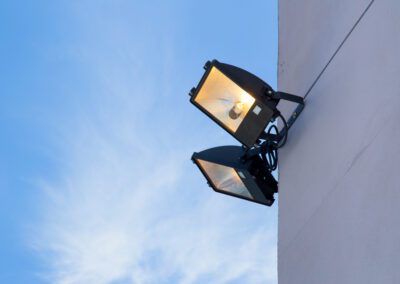 Outdoor security lights mounted on a wall against a clear sky.