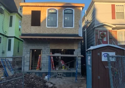 A two-story residential building under construction with exposed plywood and a portable toilet on site.