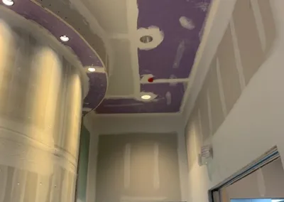 An unfinished ceiling with exposed purple insulation material and wiring above a tiled hallway.