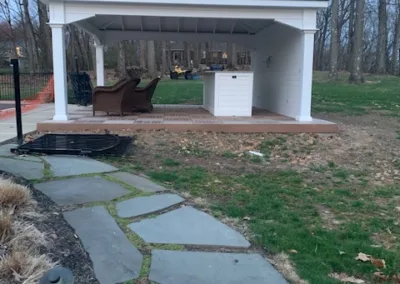 A backyard featuring a stone walkway leading to a gazebo with a bench and an outdoor piano inside.