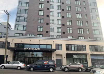 Modern apartment building at 957 broadway with parked cars in front.