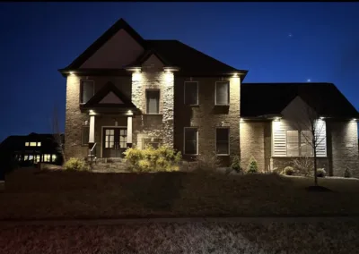 A two-story brick house illuminated by external lights at twilight.